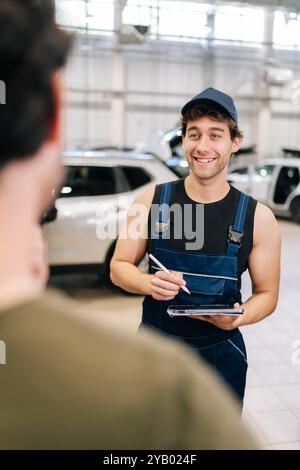 Vertikaler Schuss von der Schulter eines unbekannten Mannes-Kunden zum lächelnden Mechaniker, der die Checkliste für die Wartung und Reparatur des Fahrzeugs bei der Fahrzeugreparatur erklärt Stockfoto