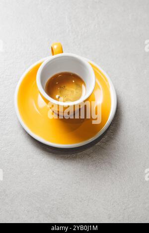 Gelbe Espressotasse gefüllt mit reichhaltigem Kaffee auf grauem Tisch mit viel freiem Platz Stockfoto