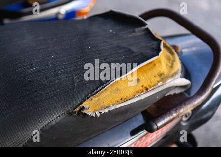 Nahaufnahme eines Motorradsitzes mit abgerissenem schwarzem Stoff, der darunter gelben Schaum freigibt. Der Sitz weist Anzeichen von Verschleiß auf. Stockfoto