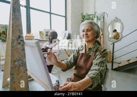 Mittlere Nahaufnahme einer Rentnerin, die mit ihrem Ehemann Pinselstriche während der Kunstsession macht Stockfoto