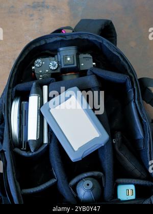 Ein offener schwarzer Kamerarucksack mit Fotoausrüstung, einschließlich Kamera, Objektiv, Festplatte und anderem Zubehör. Die Kamera ist in sichtbar Stockfoto