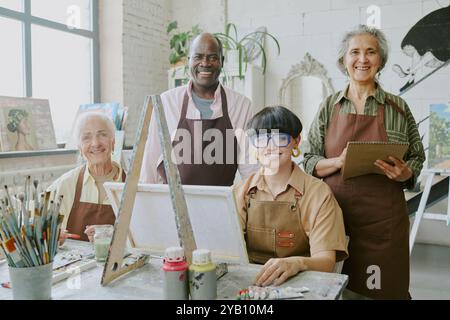Birassische Gruppe von Menschen, die daran interessiert sind, zu zeichnen, in die Kamera zu schauen und zu lächeln, während sie eine Kunsttherapie im Vintage-Studio haben Stockfoto
