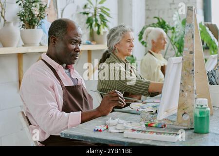 Eine kleine Gruppe von Rentnern, die während einer gemeinsamen Kunsttherapie Landschaften auf Leinwänden malen Stockfoto