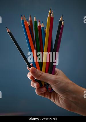 Hand hält einen Haufen Farbstifte auf blauem Hintergrund. Stockfoto