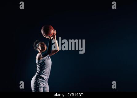 Professionelle Basketballspielerin, die Basketball vor schwarzem Hintergrund wirft. Basketballspielerin ist bereit, einen Ball zu werfen. Stockfoto