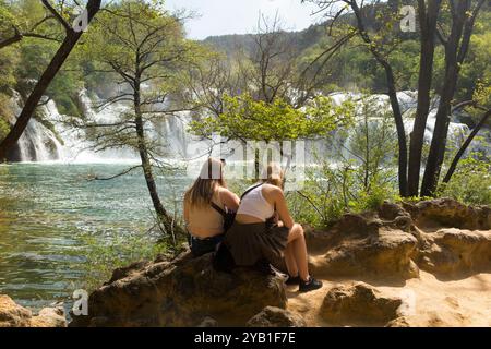 Zwei junge weibliche Besucherinnen genießen die Aussicht von einem Aussichtspunkt auf den Fluss Kirka, der über Felswasserfall / Wasserfall fließt. Krka-Nationalpark. Kroatien. (138) Stockfoto