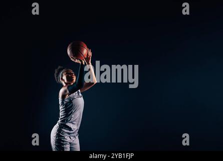 Professionelle Basketballspielerin, die Basketball vor schwarzem Hintergrund wirft. Basketballspielerin ist bereit, einen Ball zu werfen. Beruflich weiblich Stockfoto