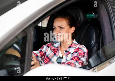 Junge weiße Frau, die ein Elektroauto fährt und lächelt. Stockfoto