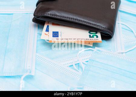 Schwarze Herren Brieftasche mit Euro Geld innen auf den blauen Einweg-medizinischen Gesichtsmasken. Handel mit medizinischen Masken. Unternehmen während einer Pandemie oder Epidemie Stockfoto
