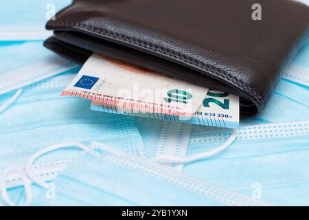 Schwarze Herren Brieftasche mit Euro Geld innen auf den blauen Einweg-medizinischen Gesichtsmasken. Handel mit medizinischen Masken. Unternehmen während einer Pandemie oder Epidemie Stockfoto