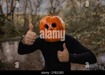 Positiver Mann mit Kürbiskopf für Halloween, der Daumen nach oben zeigt, wie eine Geste. Jack-o-Laterne Kostüm. Trick or Treat. Stockfoto