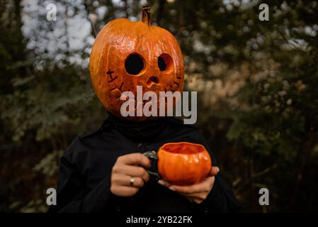 Positiv lächelnde Frau mit Kürbiskopf für Halloween Tee oder Kaffee aus Orangenbecher trinken. Jack-o-Laterne Kostüm. Trick or Treat. Stockfoto