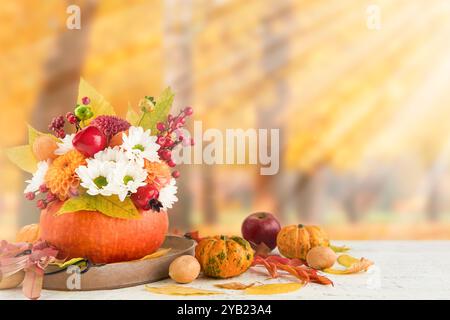 Kürbisstrauß am Thanksgiving-Tag. Herbststrauß aus schönen Blumen und Beeren in Kürbisvase auf dem Herbstwald mit Sonnenstrahlen und Blenden. Konz Stockfoto