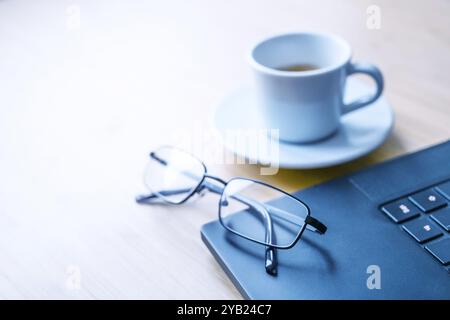 Teil eines schwarzen Laptops, Gläser und eine Tasse Kaffee auf einem Holztisch in einem Büro, Konzept für Business, Studium, Schreiben oder Journalismus, Kopierraum, sel Stockfoto