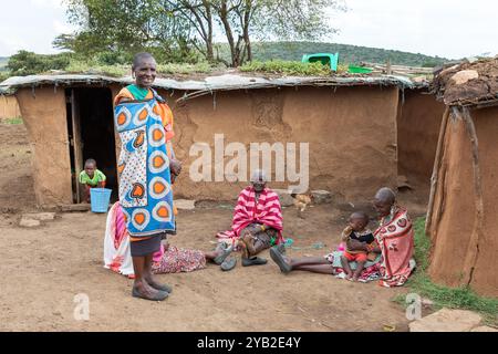 Gruppe von Masai-Frauen, die traditionelle Kostüme tragen, sitzen und plaudern vor einem traditionellen Haus aus Kuhmist und -Schlamm, Masai Village, Stockfoto