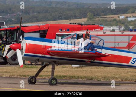 Eine Frau sitzt auf dem Flügel eines Jakovlev Yak-55 Kunstflugzeugs, das auf dem Gras des Flughafens steht. Flugschau Kosice 2024. Slowakei, Europa. Stockfoto
