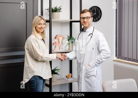 Vertikaler Schuss des jungen glücklichen, fröhlichen Arztarbeiters Therapeutin im weißen Arztgewand mit Termin, der weibliche Patientin in der modernen Klinik ho berät Stockfoto