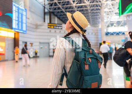 Junge kaukasische Frau mit Strohhut, Rucksack mit sich, läuft durch den Flughafen. Rückansicht, von hinten. Reisen mit dem Flugzeug, Check-in für ein Fli Stockfoto