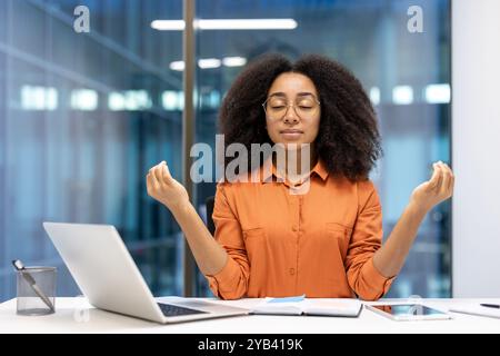 Entspannte Frau, die am Schreibtisch vor dem Laptop meditiert. Achtsamkeit üben und inneren Frieden unter der Arbeit finden. Betonung von Ruhe, Entspannung und geistigem Wohlbefinden. Stockfoto