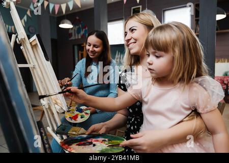 Künstlerische Bindung: Zwei Frauen und ein Mädchen malen zusammen in einem gemütlichen Atelier Stockfoto