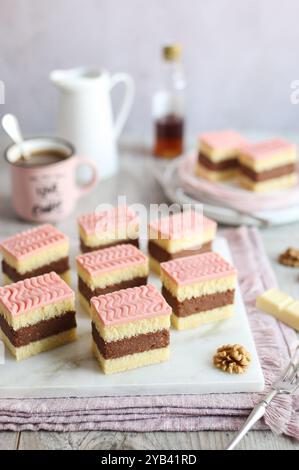 Rum-Punsch-Kuchen mit Rum und weichen Kuchenschichten mit rosafarbener Glasur. Eine Tasse Kaffee und eine Flasche Rum im Hintergrund. Stockfoto