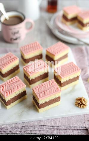 Rum-Punsch-Kuchen mit Rum und weichen Kuchenschichten mit rosafarbener Glasur. Eine Tasse Kaffee und eine Flasche Rum im Hintergrund. Stockfoto