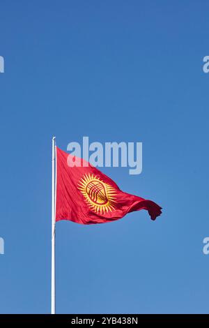 Kirgisistan aktualisierte Flagge flattert gegen den klaren blauen Himmel. Rote neue Flagge der Kirgisischen Republik auf dem Fahnenmast schwenken, echtes Foto. Kirghizia Stockfoto