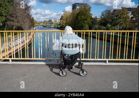 11.10.2024, Berlin, Deutschland, Europa - eine ältere Frau sitzt ganz allein im Rollstuhl auf einer Brücke und blickt über die Spree in Moabit. Stockfoto