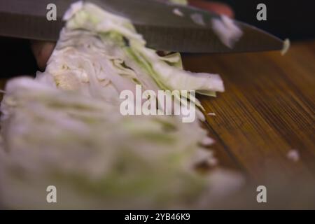 Nahaufnahme der Hände eines Küchenchefs, die akribisch frischen Kohl auf einem hölzernen Schneidebrett schneiden. Stockfoto