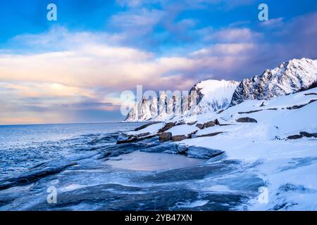 Tungeneset oder Devils Jaw Mountain auf Senja Island, Norwegen im Winter. Winterlandschaft mit schneebedeckten Berggipfeln, Fjordgewässern und Eisküste Stockfoto
