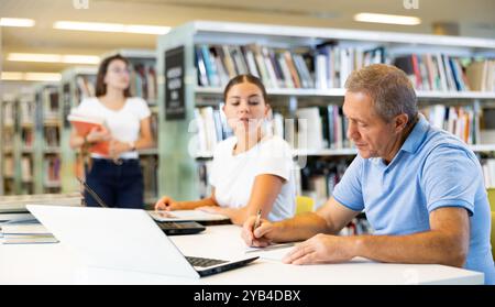 Porträt eines älteren Mannes mit Laptop und Buch in der Bibliothek Stockfoto