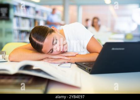 Müde Studentin schlief am Tisch in der Bibliothek ein Stockfoto