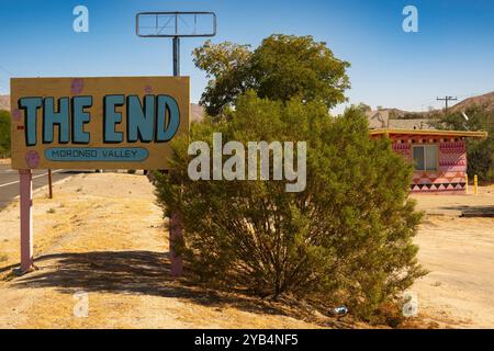 Eine seltsame Szene mit dem Endschild vor einem pinkfarbenen Gebäude und einem hohen leeren Schild in Morongo Valley, Kalifornien. Stockfoto