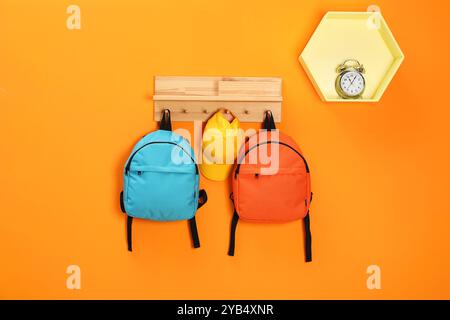 Helle Rucksäcke, Kappe und Wecker an orangefarbener Wand Stockfoto