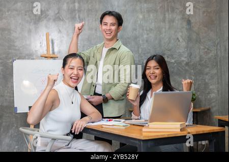 Eine Gruppe erfolgreicher junger asiatischer Startup-Teammitglieder ist in einem Meeting, zeigt ihre triumphalen Fäuste und lächelt selbstbewusst in die Kamera. bu Stockfoto