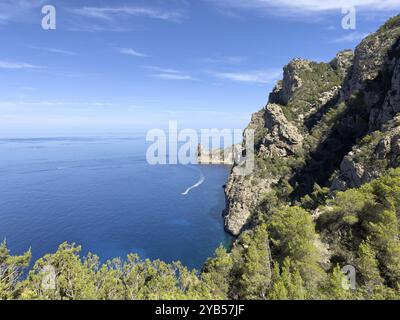 Zerklüftete Klippen mit Blick auf das tiefblaue Meer, überquert von einem Boot auf dem Wasser, Cala d'en Sardina, Ibiza, Balearen, Spanien, Europa Stockfoto