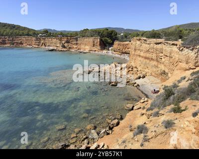 Kleiner Strand mit klarem Wasser, umgeben von hohen Klippen und Felsen in Playa es Bol Nou, Sa Caleta, Ibiza, Balearen, Spanien, Europa Stockfoto