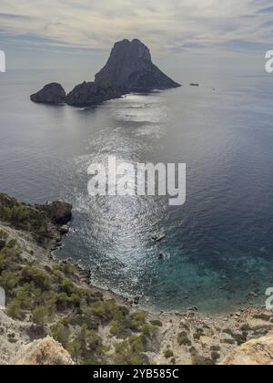 Blick auf den Inselfelsen es Vedra im ruhigen blauen Meer mit Sonnenlicht auf der Wasseroberfläche, Ibiza, Balearen, Spanien, Europa Stockfoto