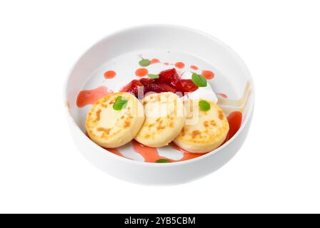 Syrniki- oder Käsepfannkuchen mit Sahnesauce und Erdbeermarmelade in weißer Platte auf weißem Hintergrund Stockfoto