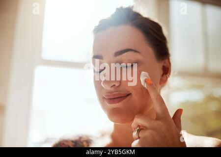 Frau, entspannen und Creme auf Gesicht für Hautpflege, Feuchtigkeit und Haut Feuchtigkeit zu Hause. Mädchen, Ruhe und Lotion im Bad für Dermatologie, Peeling und Stockfoto