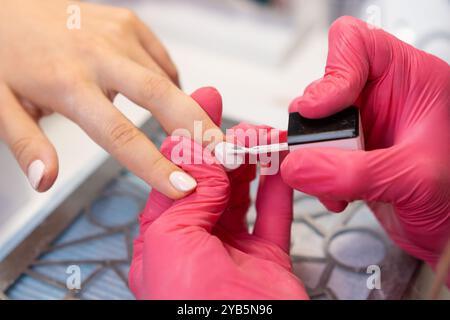 Ein erfahrener Nageltechniker in pinkfarbenen Handschuhen malt in einem gemütlichen Salon sorgfältig gellack auf die Nägel einer Frau Stockfoto