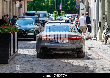 Riga, Lettland, 29. Mai 2023: Mehrere Fahrzeuge, darunter ein grauer Audi und ein schwarzes Auto, fahren eine Kopfsteinpflasterstraße hinunter. Stockfoto