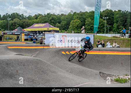 Tukums, Lettland - 10. August 2024: Ein Junge fährt mit seinem BMX-Fahrrad auf einer von Bäumen umgebenen Pumpstrecke. Stockfoto