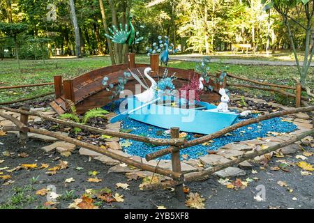 Die dekorative Parkinstallation ist von einem Holzzaun im rustikalen Stil umgeben. Eine hölzerne Brücke, ein hellblaues Boot voller Tierskulpturen Stockfoto