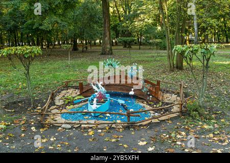 Die dekorative Parkinstallation ist von einem Holzzaun im rustikalen Stil umgeben. Eine hölzerne Brücke, ein hellblaues Boot voller Tierskulpturen Stockfoto