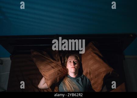 Junge Frau, die sich im Bett gestresst hat und ihre Ohren mit Kopfkissen bedeckt, fühlte sich vom lauten Lärm irritiert, während sie sich im Schlafzimmer entspannte. Schlafprobleme bei Frauen. Insomni Stockfoto