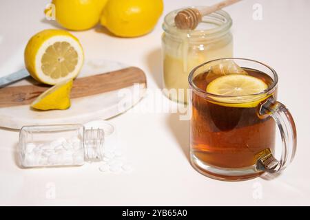 Heißer Tee mit frischer Zitrone und Honig, eine Flasche mit weißen Pillen auf weißem Tisch Stockfoto