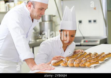 Männliche und weibliche Köche, die sich Eclairs anschauen Stockfoto