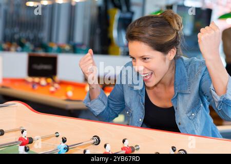 Attraktive junge Frau, die Tischfußball spielt, während sie lacht und lächelt Stockfoto