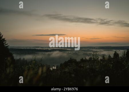 Sonnenuntergang am Horizont und malte es in wunderschönen Orangentönen. Baumkronen sind mit Nebel bedeckt. Stockfoto